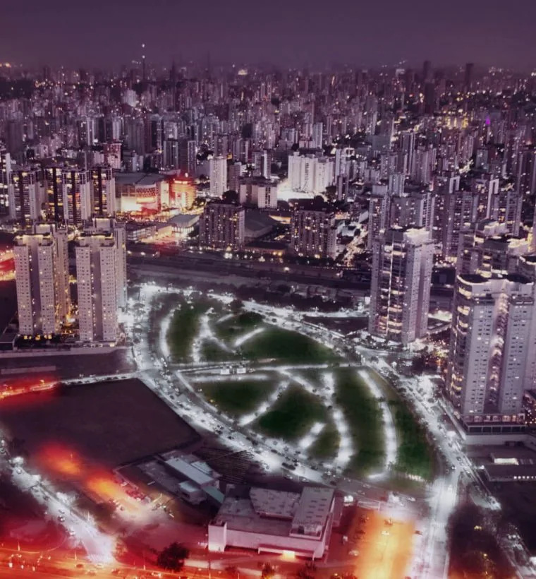 Vista aérea noturna do bairro, com o parque iluminado ao centro e a cidade ao redor