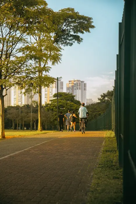 Ciclistas na ciclovia de piso intertravado que contorna o parque, entre árvores