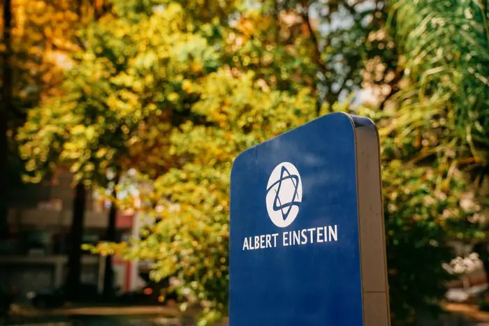 Placa de identificação do Hospital Albert Einstein entre as árvores da calçada