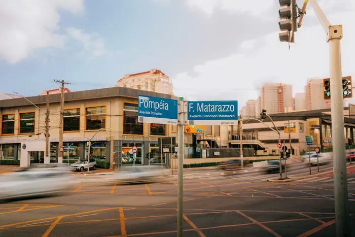Cruzamento sinalizado com as placas das avenidas Pompeia e Francisco Matarazzo, com carros passando