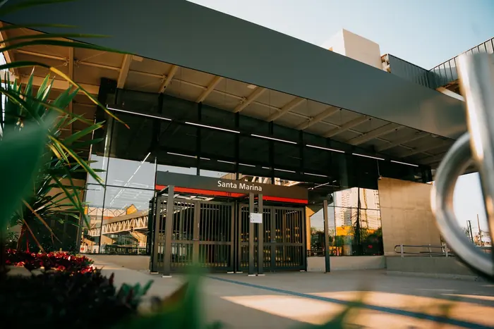 Entrada da estação Santa Marina ao entardecer, com o letreiro sobre os portões de vidro e a passarela metálica ao fundo