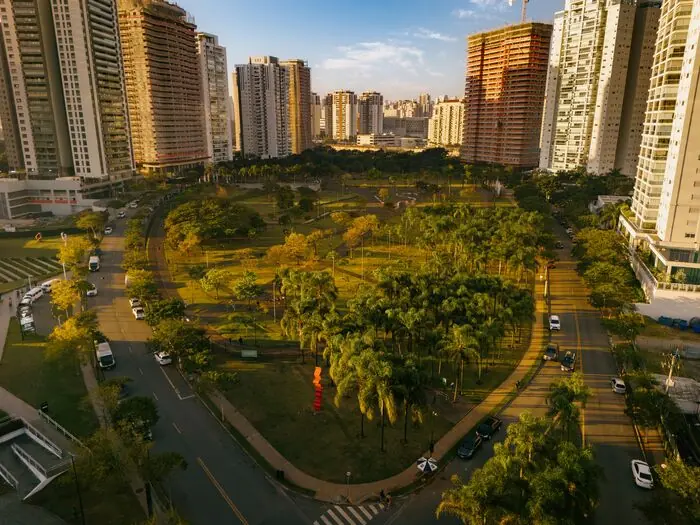 Vista aérea do parque ao entardecer, com a avenida arborizada contornando o gramado