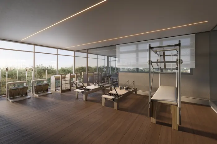 Sala de pilates com aparelhos de madeira sobre piso de tábua corrida e janelas do chão ao teto