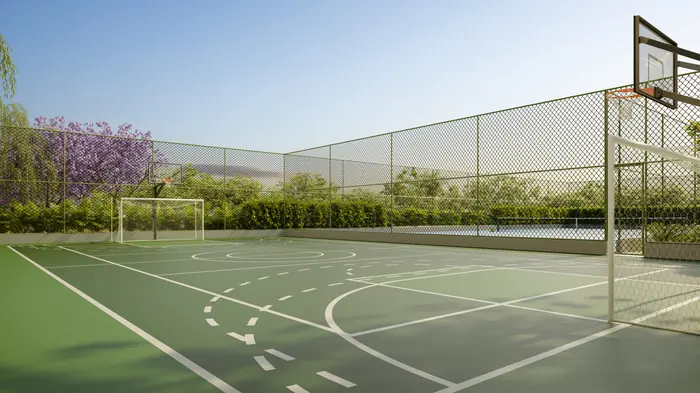 Quadra poliesportiva verde com trave de futebol e tabela de basquete, cercada por alambrado e jacarandás